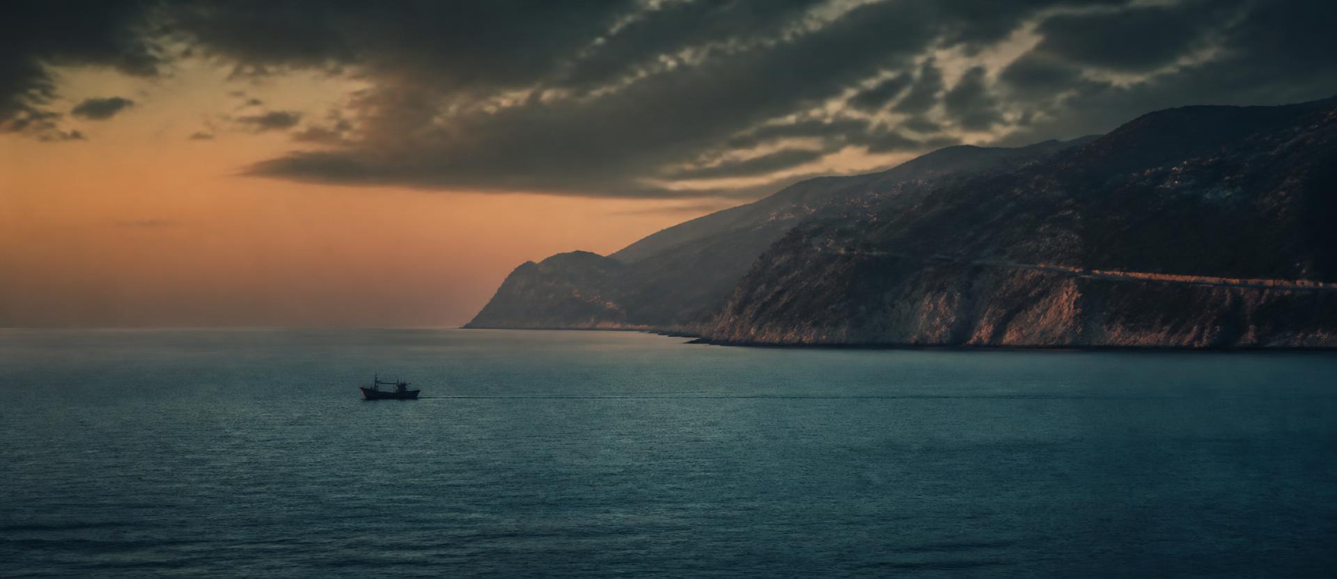 Dramatische mediterrane Küste bei Sonnenuntergang mit einem einzelnen kleinen Boot auf dem ruhigen Meer